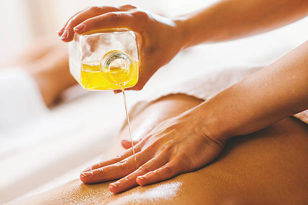 donna versare olio per massaggio nella spa client - olio per massaggi foto e immagini stock