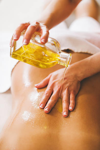 donna versare olio per massaggio nella spa client - olio per massaggi foto e immagini stock