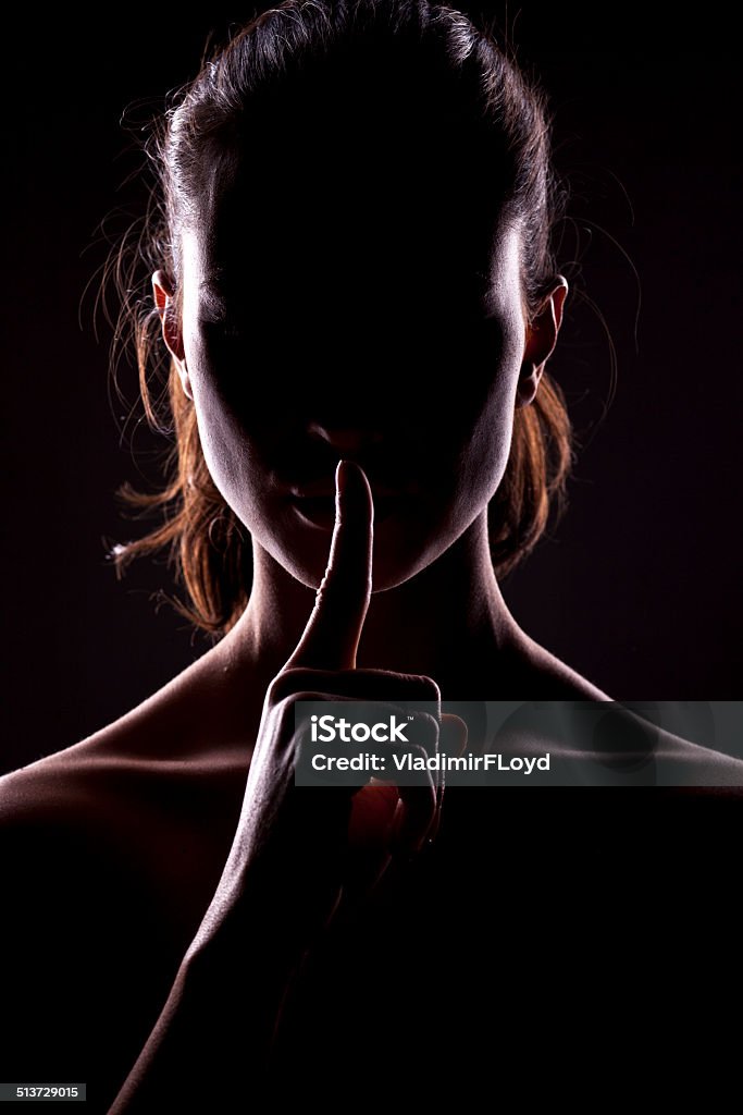 taboo unknown woman with the face in the shadow holding finger on lips Finger on Lips Stock Photo