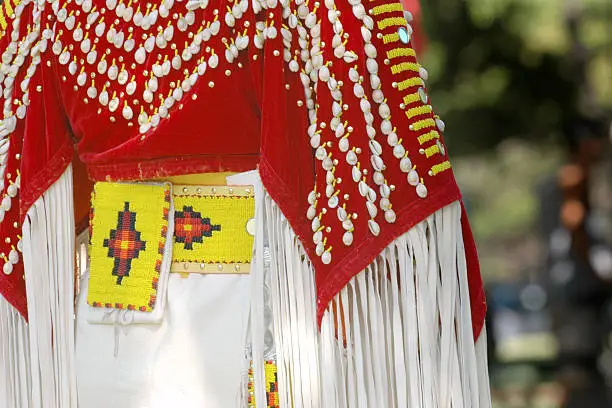 Close-up of a colorful traditional American Indian costume with shell beading, red with white fringe and yellow accents.