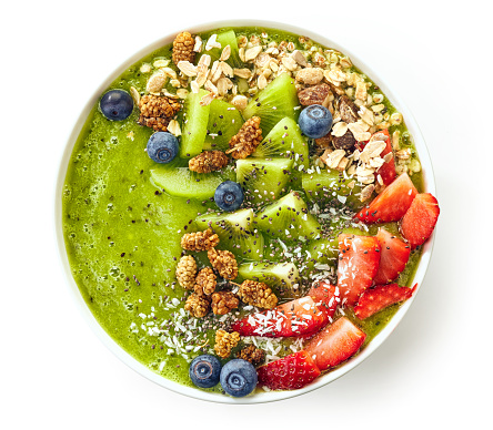 breakfast kiwi smoothie bowl topped with oat flakes and berries isolated on white background, top view