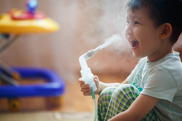 kleine junge macht einatmen zu hause, die medikamente, die anfälligkeit - asthmatic child asthma inhaler inhaling stock-fotos und bilder