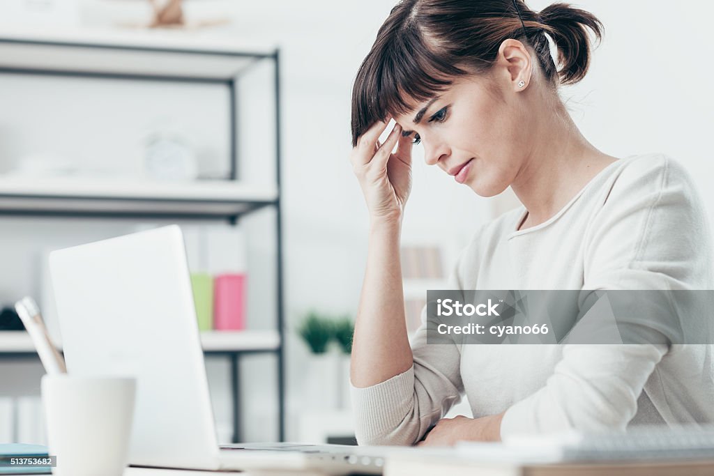 Woman with headache in the office Sad tired woman having a bad headache, she is sitting at office desk and touching her temple Adult Stock Photo