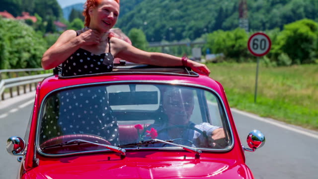 An older lady is enjoying a car ride in a red yugo