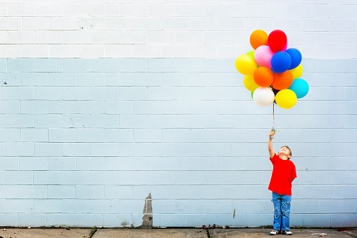 Little boy standing against the wall with a lot of colorful balloons.
