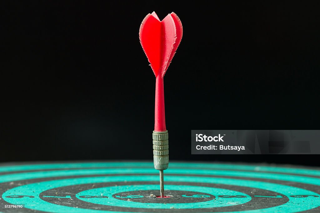 Dart arrow hitting in the center of green dartboard. Red dart arrow hitting in the center of green dartboard. Bull's-Eye Stock Photo