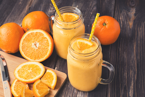 Orange fruit smoothie in the glass jars with fresh orange slices on rustic wooden background. Vintage toned picture.