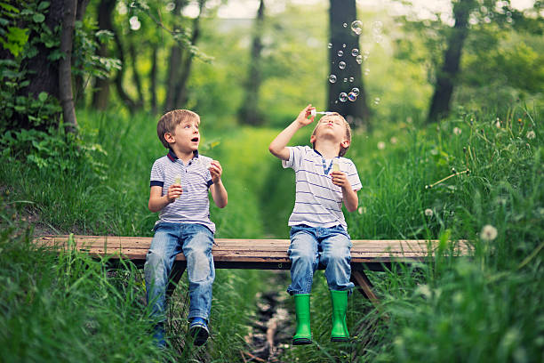 Little brother blowing  bubbles on a little bridge in forest