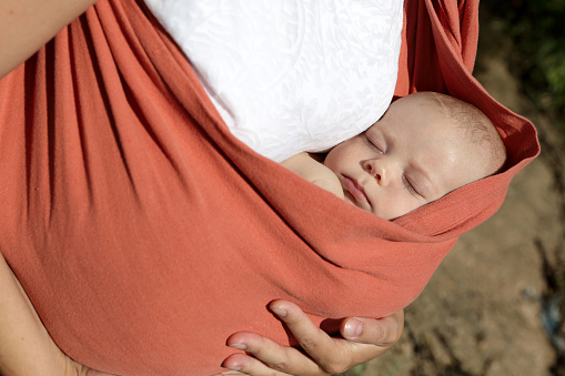 Newborn sleeping in the orange baby sling carrier outdoor