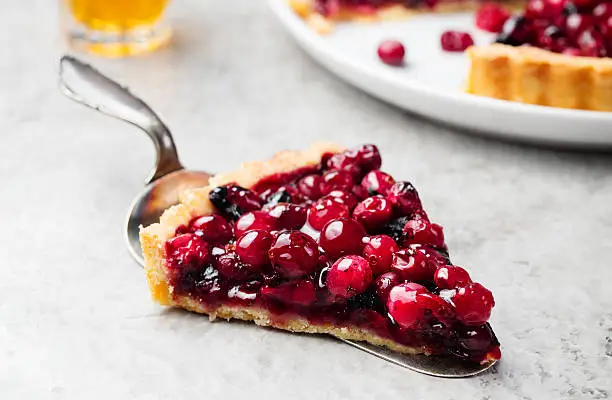 Tart, pie, cake with jellied fresh cranberries, bilberries and winter spices on a grey stone background. Copy space