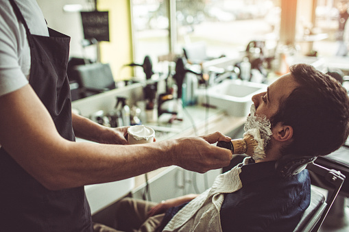 Photo of a young man, siting in a barber's chair in a little barber's shop waiting for his shave 