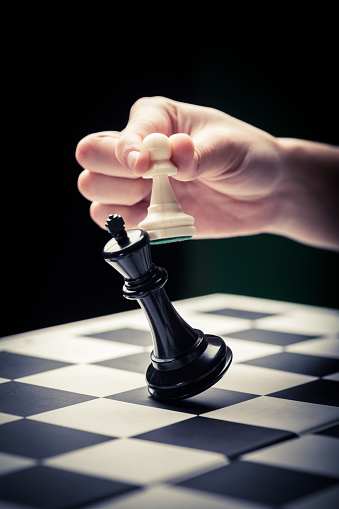 Close-up image of a hand moving a chess piece and defeating the challenger.