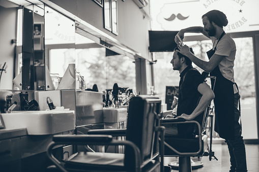 Photo of a young man and his barber, sitting in a barber's chair in a little barber's shop waiting for his haircut 