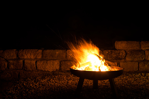 Burning stack of wood in a fire bowl made of steel in a warm summer night. Nice little campfire in the garden.