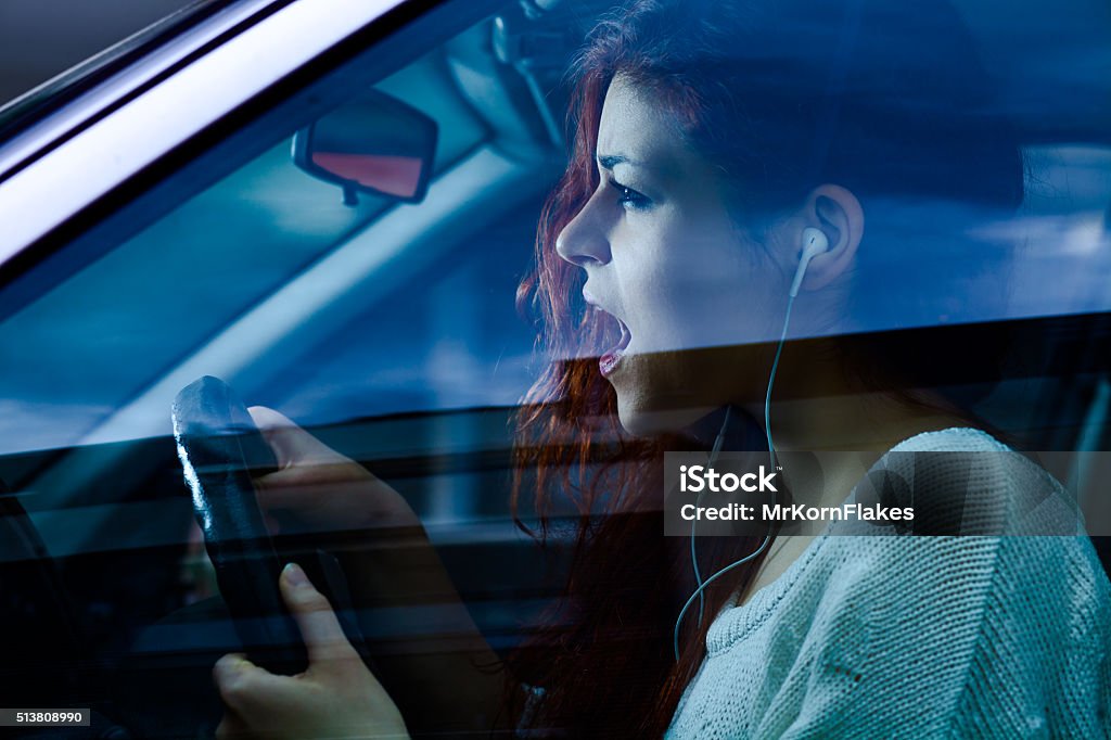 Woman Driving a Car Screaming Woman with Earbuds Driving a Car Singing Stock Photo