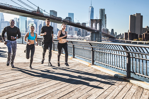 Group of healthy mixed race people running in DUMBO - New York City - USA. They are running in the city streets wearing professional sport clothes.