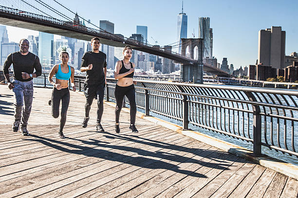 Urban runners - New York - Brooklyn Bridge Group of healthy mixed race people running in DUMBO - New York City - USA. They are running in the city streets wearing professional sport clothes. dumbo new york photos stock pictures, royalty-free photos & images