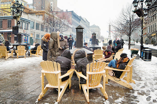 Group of people warming up around public fireplace Old Montreal Montreal, Canada - February 6, 2016: Group of people warming up around public fireplace while visiting Place Jacques-Cartier in Old Montreal. Snow is falling all around them. place jacques cartier stock pictures, royalty-free photos & images