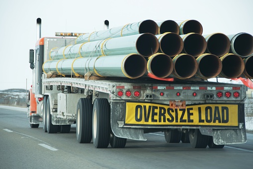 Oversize Load sign on back of truck carrying steel or fiberglass pipes.  