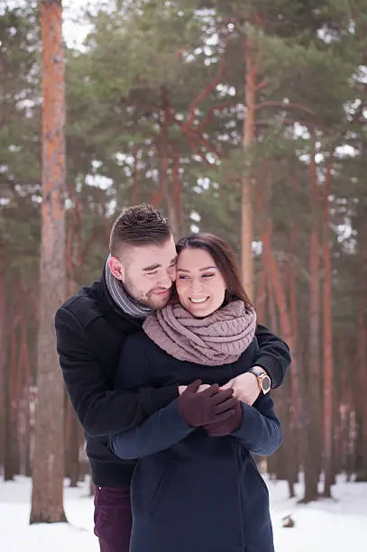 A loving couple walking in winter park with pine trees.
