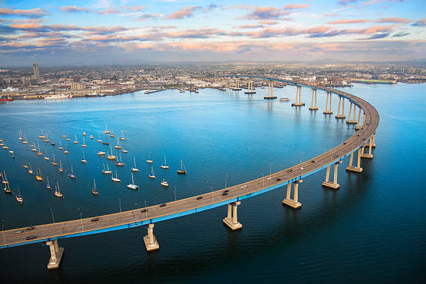 San Diego Coronado Bay Bridge From Above The unique curvature of the Coronado Bay Bridge spanning San Diego Harbor joining two cities; San Diego and Coronado. I shot this image at dusk after a winter storm from a helicopter during a chartered photo flight at about 300 feet elevation. jetty aerial stock pictures, royalty-free photos & images