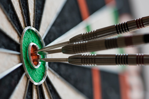 Closeup view of silhouette of three darts sticking in a professional sisal dartboard. All three darts hit the inner bull / bull's eye / mark.