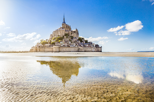Panoramic view of famous Le Mont Saint-Michel tidal island on a sunny day with blue sky and clouds, Normandy, northern France.