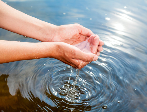 Woman taking clear water at a lake by hands