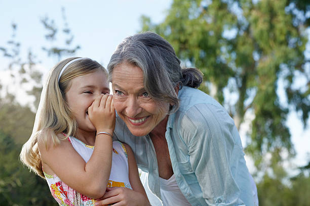 Girl Whispering In Grandmother's Ear Closeup of a young girl whispering in grandmother's ear outdoors whisperer pictures stock pictures, royalty-free photos & images