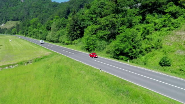 Two modern cars passing a small red vintage car