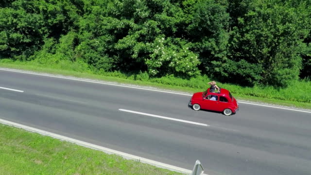 Red vintage car driving on a country road. The woman is standing up