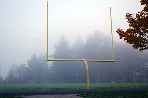 Empty football field with yellow goal post in autumn with morning fog