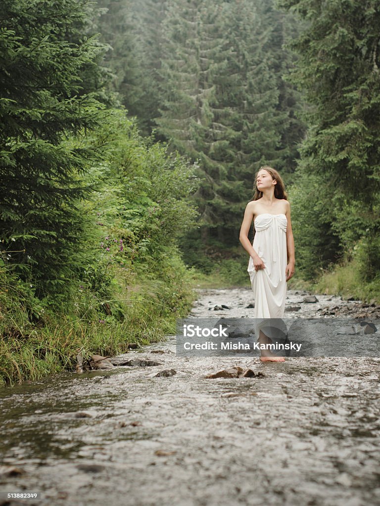 Young woman goes barefoot through the mountain river Young woman goes barefoot through the mountain river in rainy weather Active Lifestyle Stock Photo