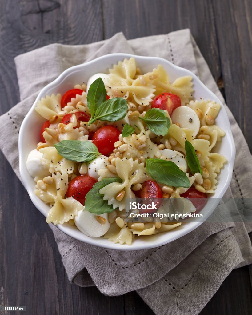 Pasta salad with tomato, mozzarella, pine nuts and basil Pasta salad with tomato, mozzarella, pine nuts and basil in a white ceramic bowl on a wooden table Bow Tie Pasta Stock Photo