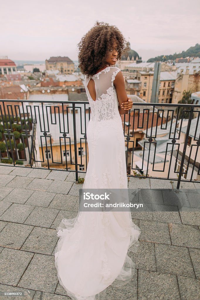 Charming african bride in white lace wedding dress looks over Charming african bride in white lace wedding dress looks over shoulder to the camera. Adult Stock Photo