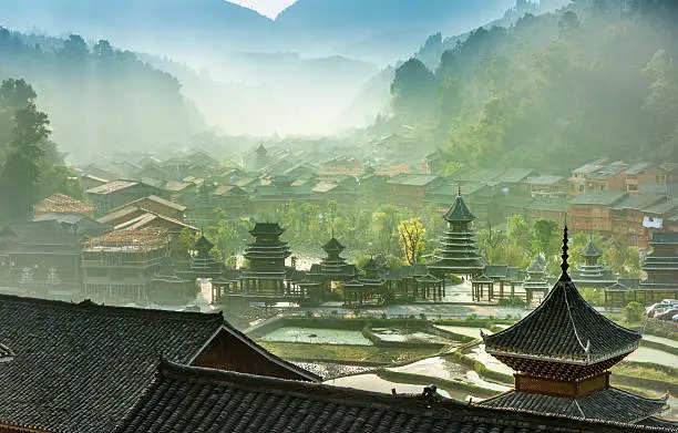 Sunrise,fog, Rice paddy in the front, village and mountains in the back. Roof of a temple in front.