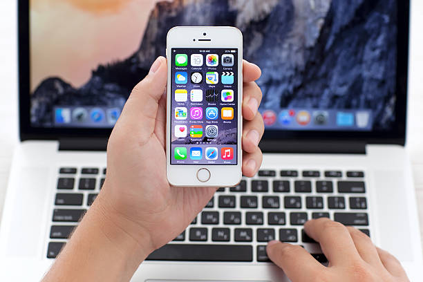 iPhone 5S with IOS 8 in hand over MacBook Pro stock photo