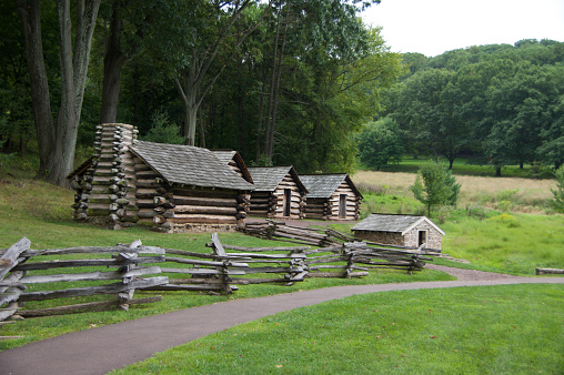 A small log cabin village with a rail fence in the foreground and a forest in the background.