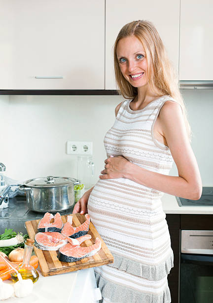 istock Pregnant woman cooks salmon 513918357