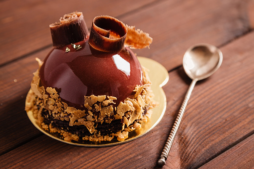 French mousse cake covered with chocolate glaze on wooden background. Modern european cake pastry. Shallow focus