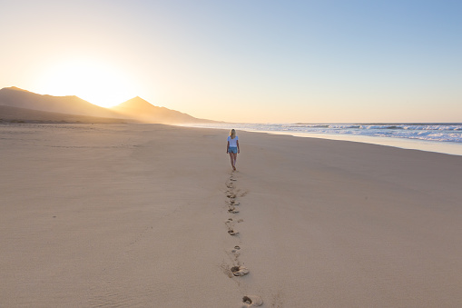 Woman walking on sandy beach in sunset leaving footprints in the sand. Beach, travel, concept. Copy space.