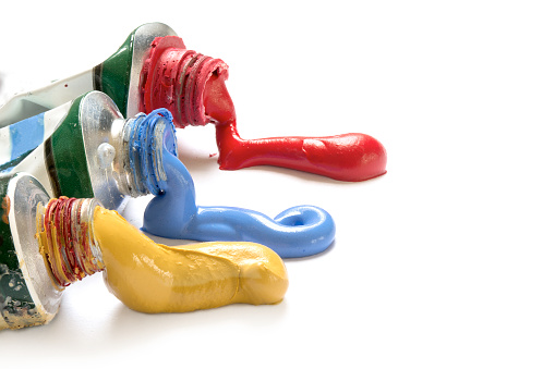 paint colors in yellow, blue and red flowing from the tubes, closeup isolated with shadow on a white background with copy space