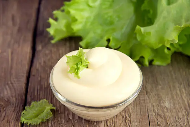 Fresh tasty mayonnaise sauce in bowl on rustic wooden background, close up, horizontal