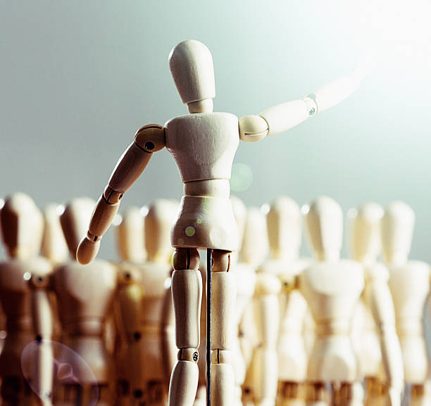 Wooden puppet addressing audience of other puppets A little wooden figurine with its arm raised addresses an out-of-focus audience of other wooden puppets at a rally, meeting, seminar or social occasion, or he could be a choir master leading them in a choral performance. singer back stock pictures, royalty-free photos & images
