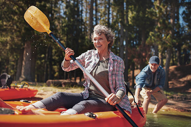 Mature couple enjoying a day at the lake with kayaking Portrait of happy senior paddling kayak in the lake with man supporting from behind. Mature couple enjoying a day at the lake. active lifestyle stock pictures, royalty-free photos & images