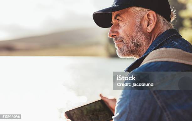 Mature Man Wearing Cap Sitting At A Lake Stock Photo - Download Image Now - Men, Contemplation, Mature Men