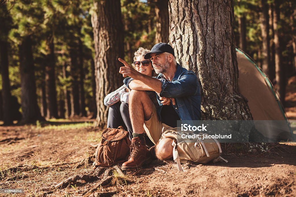 Senior hikers camping in forest Portrait of mature couple relaxing at their campsite with man showing something to woman. Senior couple hiking and camping in forest on a summer day. Hiking Stock Photo