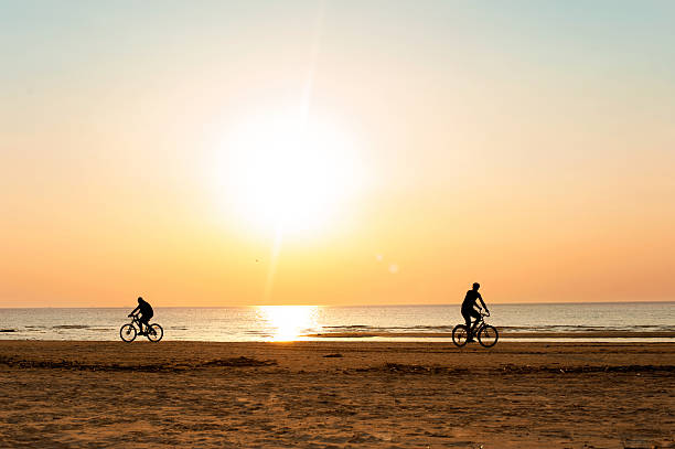 istock Men cyclists silhouettes at summertime sunset background on the beach. 513945520