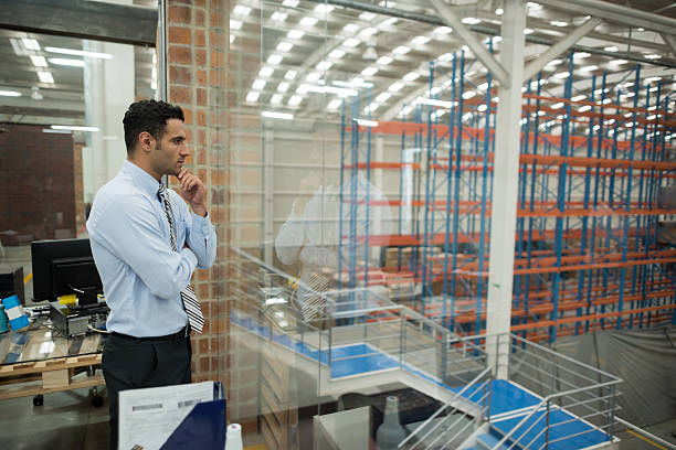 Business man working on freight transportation Business man at the office working on freight transportation and overlooking a warehouse warehouse office stock pictures, royalty-free photos & images