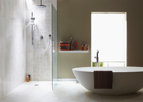 The interior of a simple, modern bathroom in a cool, green tone. There is a bath, shower, a bath towel . There are light grey tiles in the shower with running water